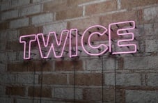 A pink neon twice sign on a stone wall