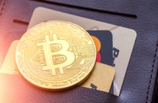 A close-up image of a leather wallet with bank cards and a gold Bitcoin coin