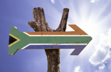 A wooden sign of an arrow painted with the South African flag against a sunny blue sky 