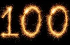 An image of glowing sparkler numbers 100 on a dark background with bright golden light trails and sharp contrast detail