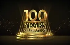 An illustration of a golden '100 Years' text on pedestal with spotlights and sparkles on a dark background.