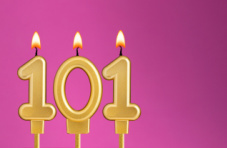 Three lit golden 101 birthday candles on a pink background