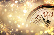 A closeup of a clock with the dials counting down to 2024 surrounded by golden fireworks 