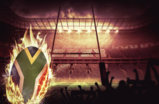 A rugby ball in flames covered in the South African flag on a rugby field in a full stadium at night