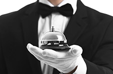 A closeup photgraph of a bellboy wearing a tux and white gloves holding a silver bell isolated on white