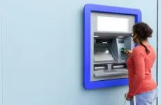 A photo of a woman withdrawing money from an ATM at a light blue building