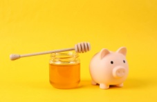 A photo of a pink piggybank next to a jar of honey on a yellow background