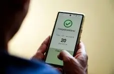 A photograph of a person holding a smartphone showing a "Congratulations! You've earned 20 points" screen on a warm background