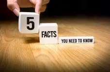 A photograph of a hand placing white blocks spelling "5 Facts You Need To Know" in descending steps on a wooden surface 
