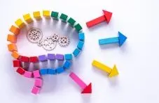 A photograph of colourful wooden blocks forming a magnifying glass shape with gears and arrows on a white background