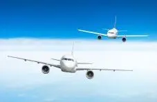 A photo of two white passenger jets flying in close formation above a thick bank of cloud, seen head-on against a clear blue sky