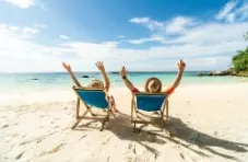A photo of two people lying on a sandy beach on beach chairs having a good time looking at the blue sky and ocean