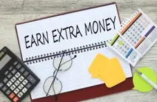 A photo of an open notebook, with EARN EXTRA MONEY printed in black,  next to a calculator, specs, pen and calendars.