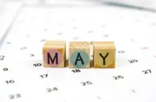 A photograph of wooden blocks spelling May on a calendar page with dates visible on a soft white background