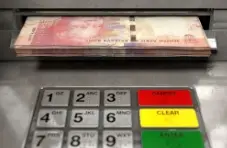 A close-up photo of an ATM dispensing a wad of fifty rand bills