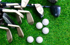 A photograph of a golf bag, golf clubs and balls lying on a green grass golf course