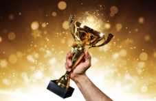 An image of a male hand holding a trophy in the air on a sparkly golden background