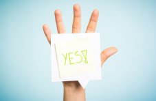A photo of an open hand showing five fingers with a sticky note readying ‘yes!’ on a blue background
