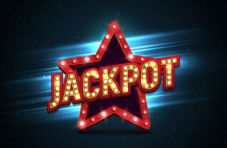 An illustration of a red star and the word ‘jackpot’ across it in red and gold with show lights on a dark background