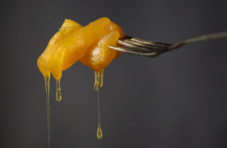 A koeksister dripping with syrup on a fork against a dark grey background