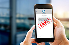 A photo of a lady holding a smartphone with a blurred message and a “FAKE” stamp across it on a blurry office-looking background