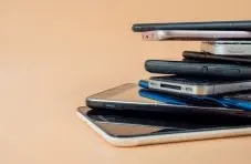 An illustration of a stack of various smartphones piled on top of each other against a warm beige background