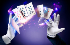 Magician hands in white gloves doing a card trick on a dark background with purple light