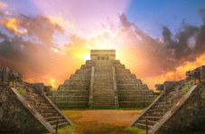 A photo of ancient Aztec pyramids set against a partially cloudy sky at sunset