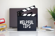 A movie clapper with the text ‘helpful tips’ in white chalk in front of a laptop on a desk against a white wall