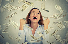 A photograph of a delighted young woman with Dollar notes raining down on her on a light greyish background