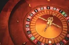 A close-up photo of a wooden roulette wheel with gold spinner, numbered pockets and a white ball resting inside