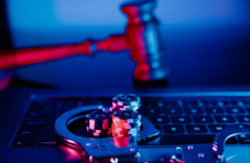An image of a gavel being held over a laptop with poker chips and handcuffs on the keyboard