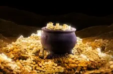 An illustration of a black cauldron overflowing with gold coins on a dark background