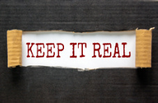Torn black cardboard revealing red typed words “keep it real” on white
