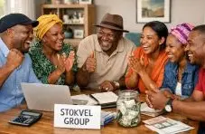 A photograph of six joyful people around a table with a "Stokvel Group" sign, laptop and money jar on a home interior backround 