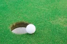 A photograph of a white golf ball on the edge of a hole on a green grass background