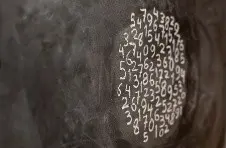 A photo of a series of numbers written in white chalk on a black board in a circular shape