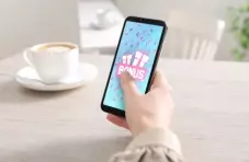 A photo of a person holding a mobile bonus with a bonus offer on sitting at a table with a cup of coffee