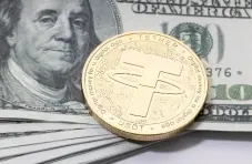An image of a physical golden Tether coin, placed upon a stack of US dollar notes.