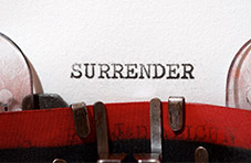 A photo of the word surrender in typical typewriter font on a piece of paper inserted into a red vintage typewriter