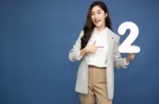 A photo of a young woman holding a large white 2 in one hand and pointing to it with the other 