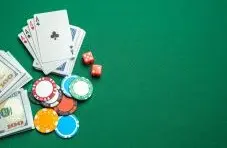 A close up photo of poker cards showing four aces, sitting next to red dice and gambling chips on a green felt background
