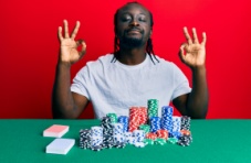 An image of a relaxed man smiling sitting at a table with poker chips against a red background 
