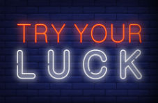 An illustration of a neon lit slot machine with the word ‘casino’ above it and ‘try your luck’ to the left on on dark brick wall