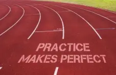 A photo of a maroon running track with the words “practice made perfect” printed across the lanes