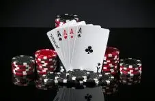 A photograph of four aces and a joker card surrounded by stacked red and black poker chips on a dark background