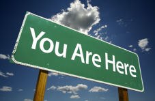 A green road sign saying ‘you are here’ in white text against a blue sky background