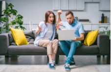 couple sitting on the sofa hands in the air celebrating their video poker win on their laptop