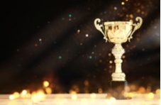 An image of a gold trophy on a wooden table with abstract shiny lights on a dark background