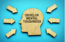 A head shape carved from wood with the words mental toughness on it and arrows pointing at it against a blue background